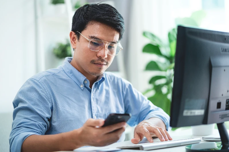 Blog 2 A man wearing glasses is sitting at a desk with a computer and a cell phone